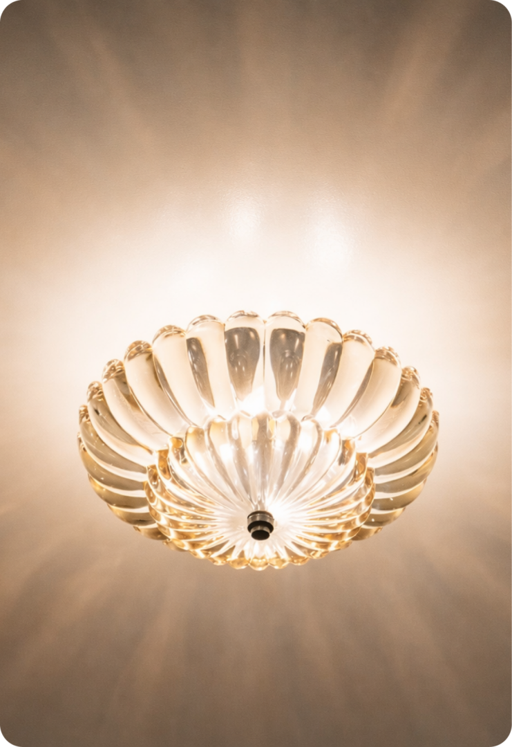 A glass ceiling light fixture glows warmly, casting soft, radial light patterns on the ceiling. The fixture has a wavy, bowl-like shape with a metallic center.