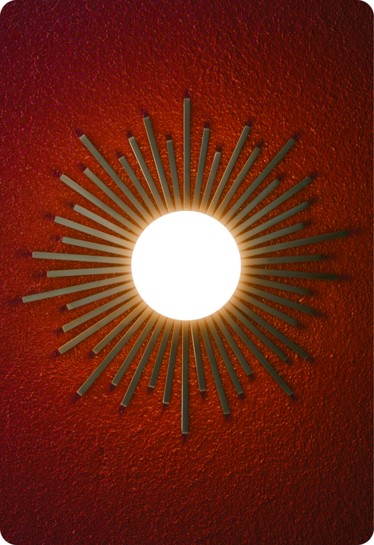 A sunburst-style wall light with metallic rays radiating from a bright central circle, mounted on a textured red wall.