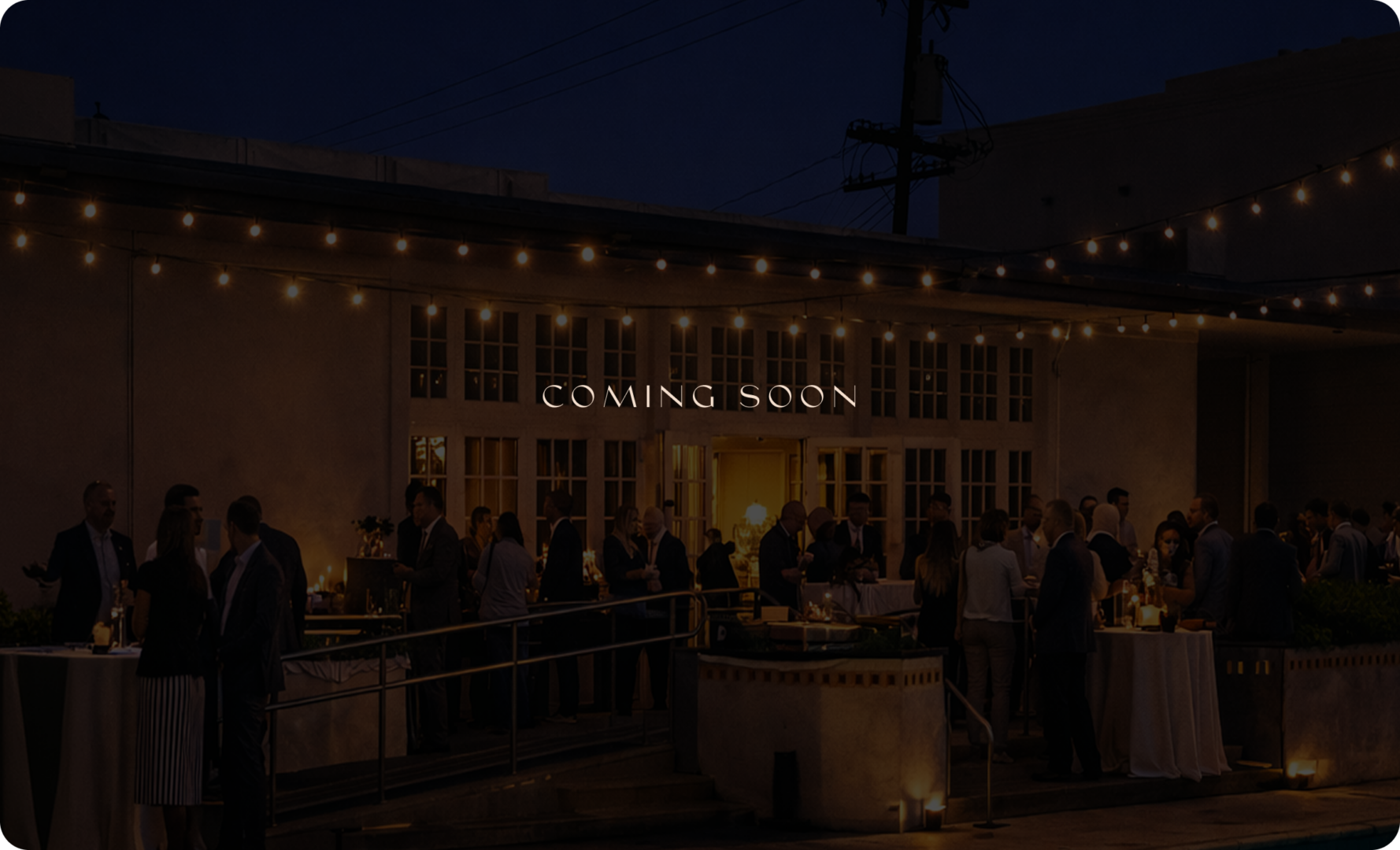 Outdoor evening event with people socializing under string lights in front of a building; COMING SOON text is illuminated above the entrance.
